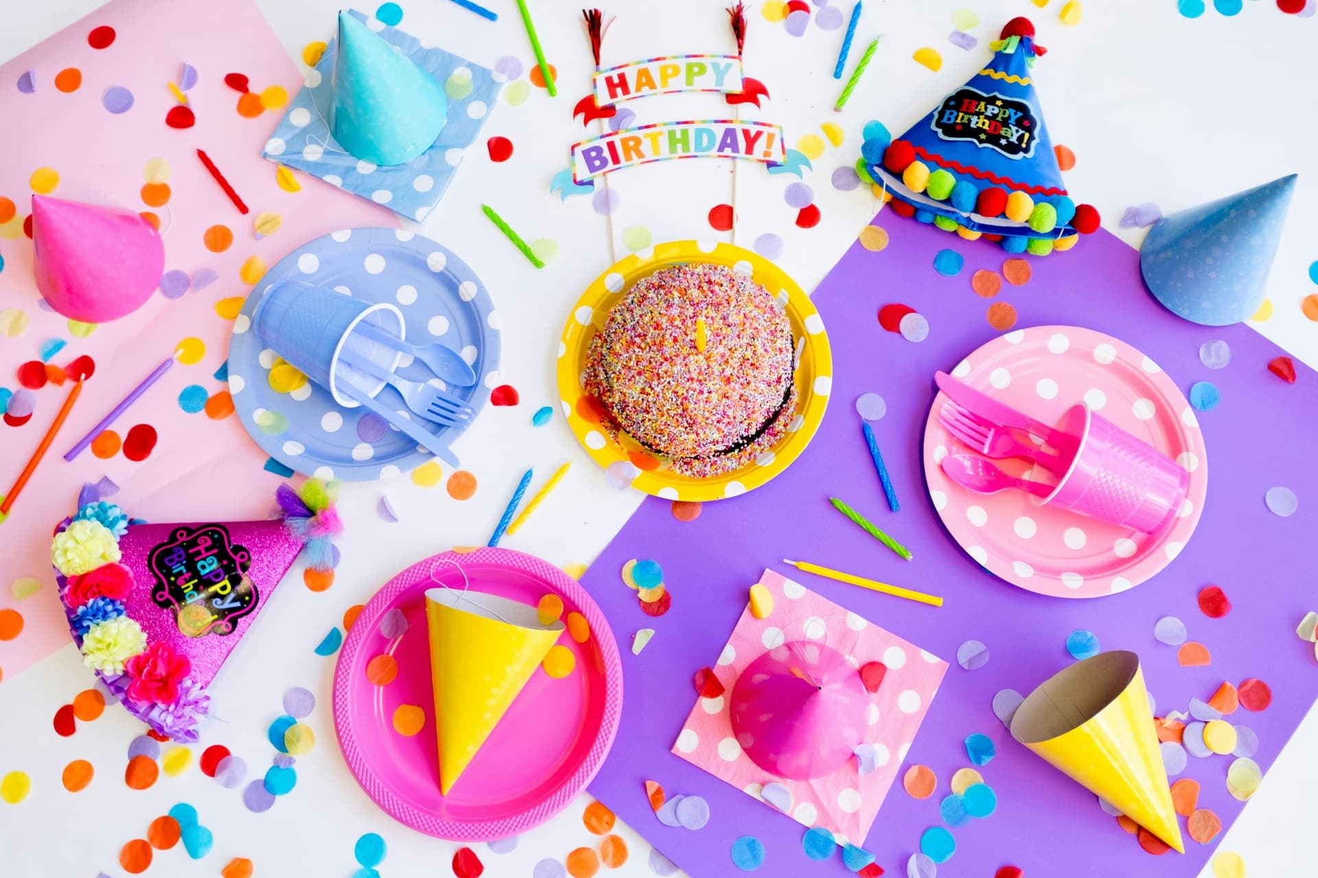 Colorful birthday party table with cake, hats and confetti